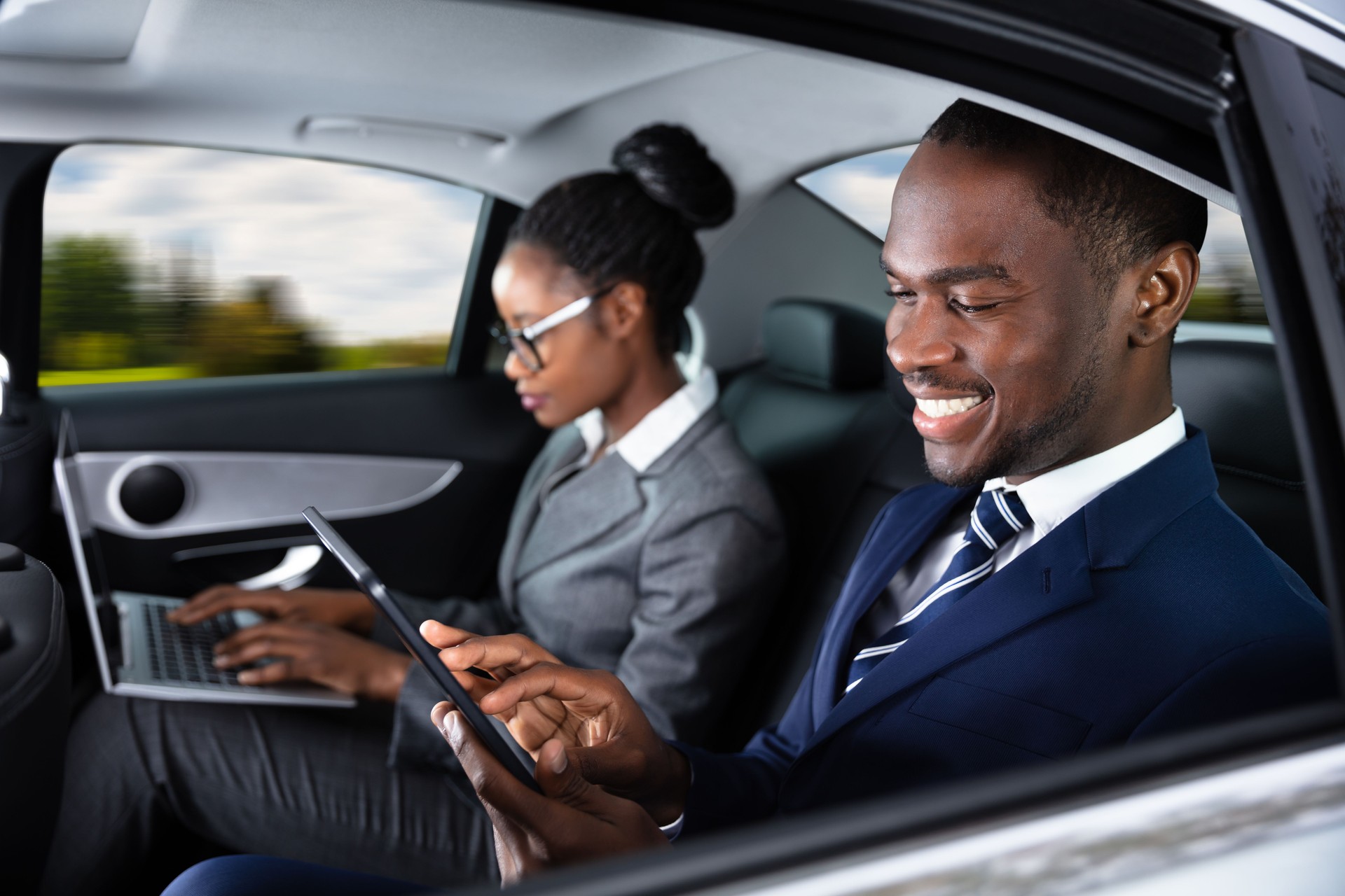 Two Businesspeople Sitting Inside Car Using Electronic Devices